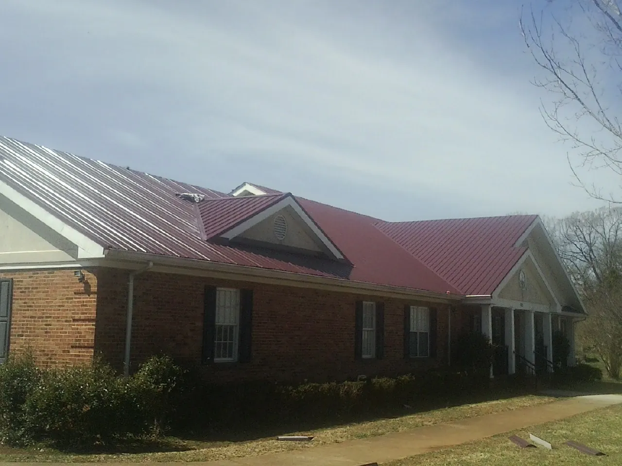 Red metal roof with gabled entries on a long brick building, from a Hail Damage Roof Repair job in Kent City