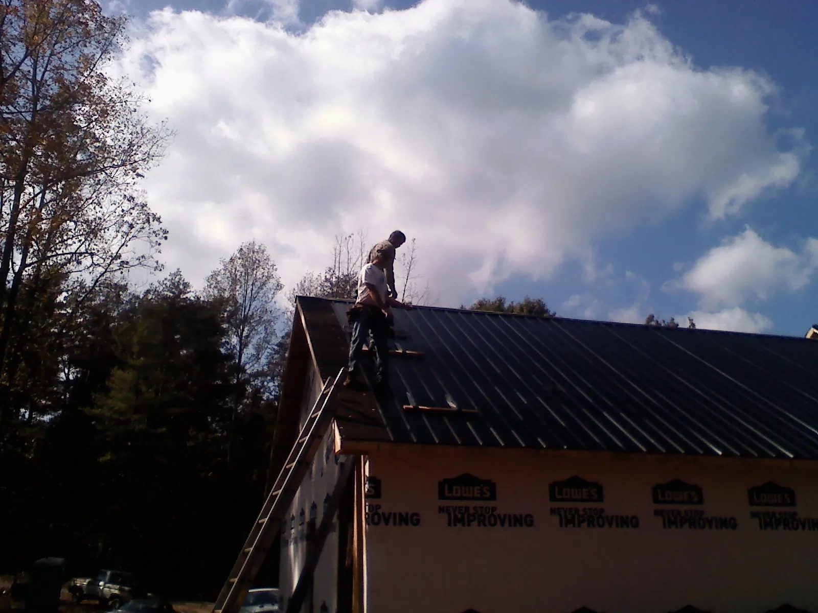 Roofer fastening dark metal panels high against a cloudy sky, from a Roof Inspection job in Kent City
