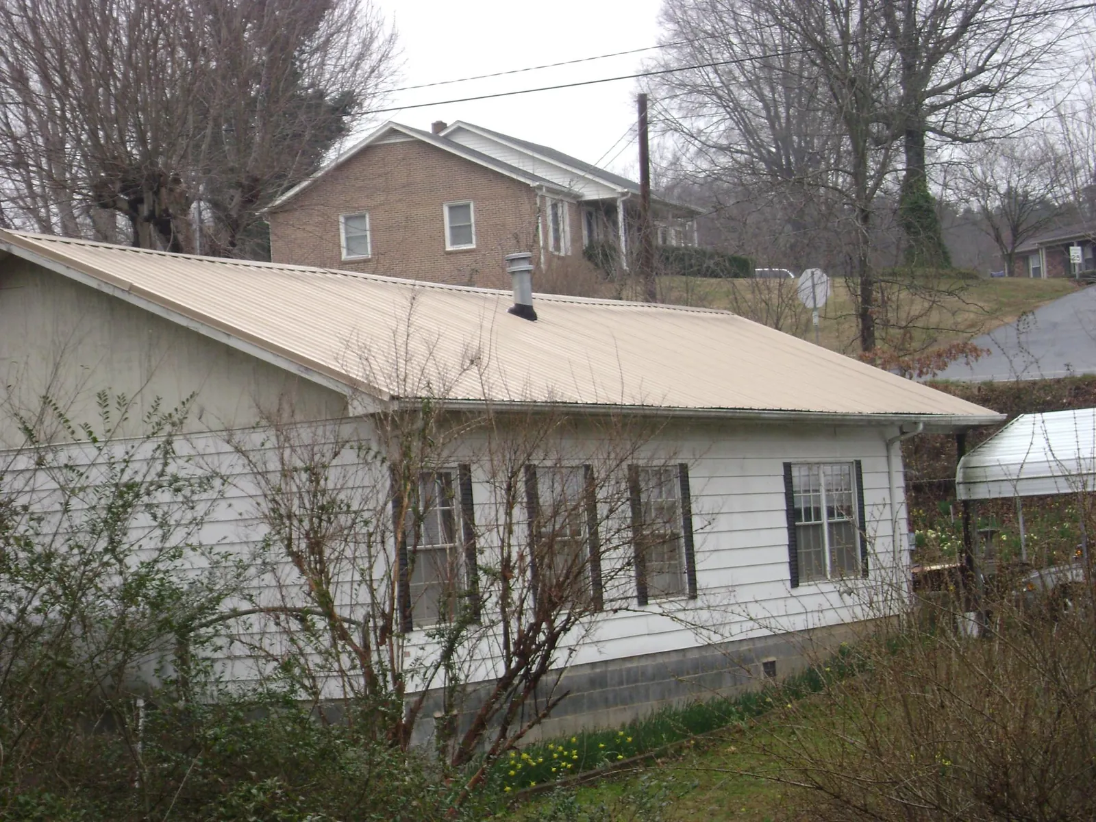 Tan metal roof on a white sided house set into a hillside — Commercial Roofing by Roofing Brothers in Kent City